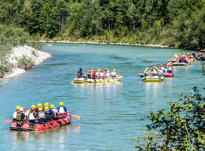 Raftinggruppen im Salzburger Land paddeln auf einem klaren Fluss zwischen Waldlandschaft © Shutterstock
