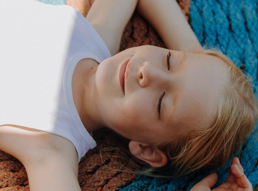 Wohlfühlmomente für kleine Gäste im Familienhotel Botenwirt – Ein entspanntes Kind liegt mit geschlossenen Augen auf einer Decke und genießt die Sonne