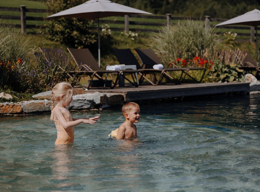 Zwei Kinder spielen und schwimmen im Naturbadeteich des Familienhotels Botenwirt