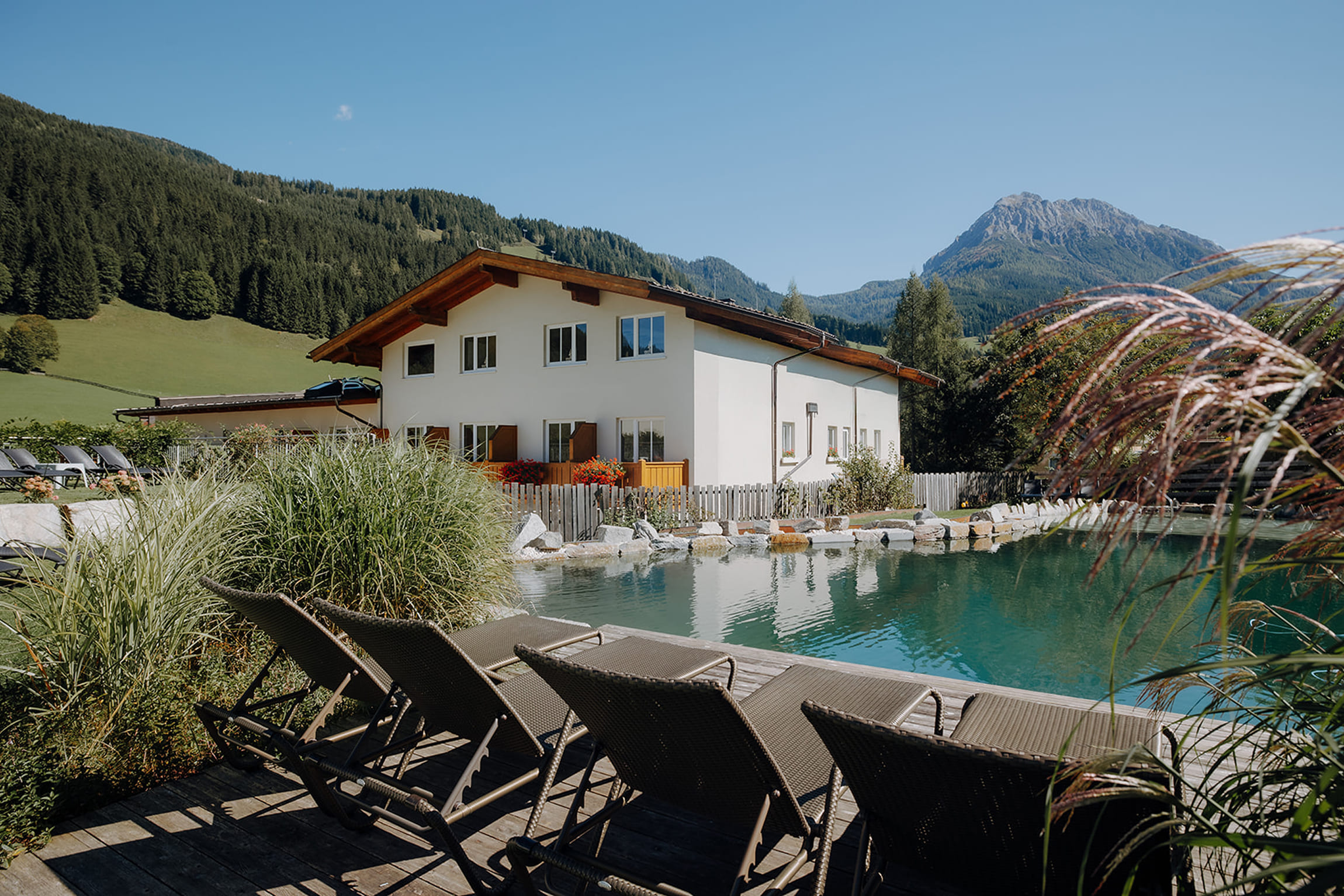 Liegestühle und Sonnenschirm am Naturbadeteich des Familienhotels Botenwirt – ruhige Wohlfühlatmosphäre direkt am Wasser