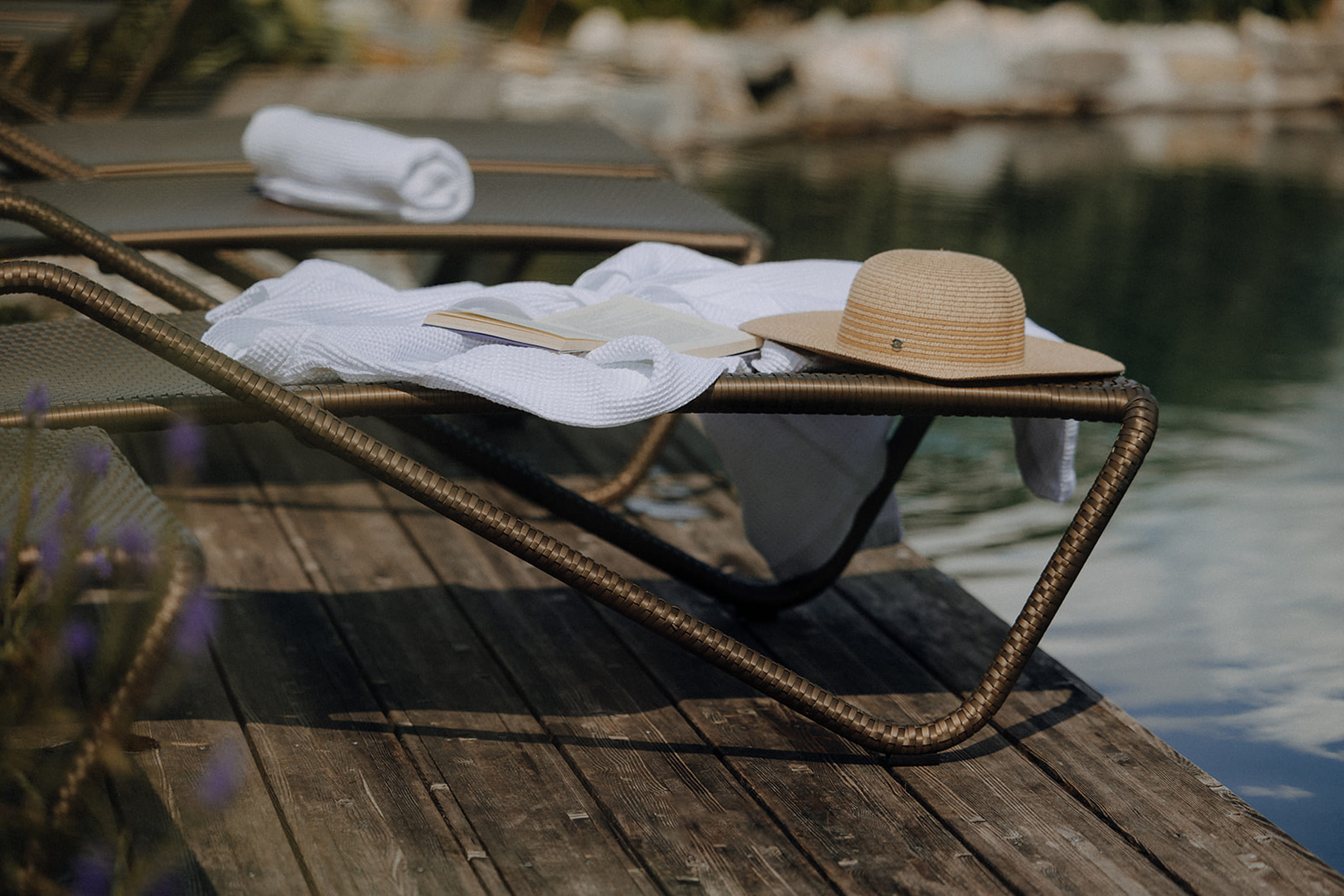 Entspannungsplatz am hoteleigenen Badeteich – Liegestuhl mit Handtuch, Buch und Sonnenhut auf einem Holzsteg am Wasser