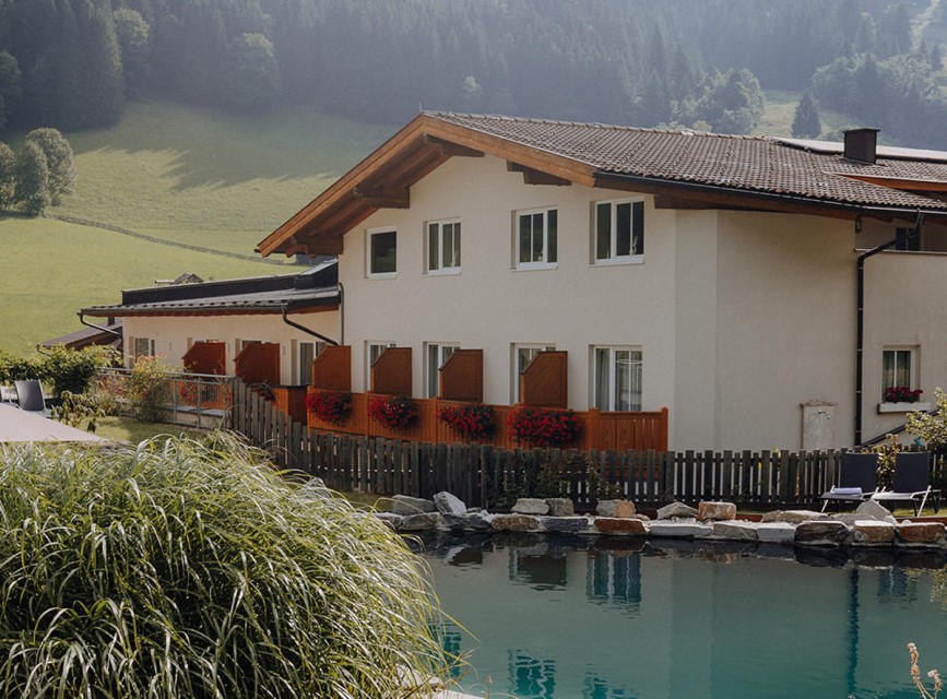 Außenansicht des Hotels Botenwirt mit Naturbadeteich und Blick auf die grünen Berge in Kleinarl