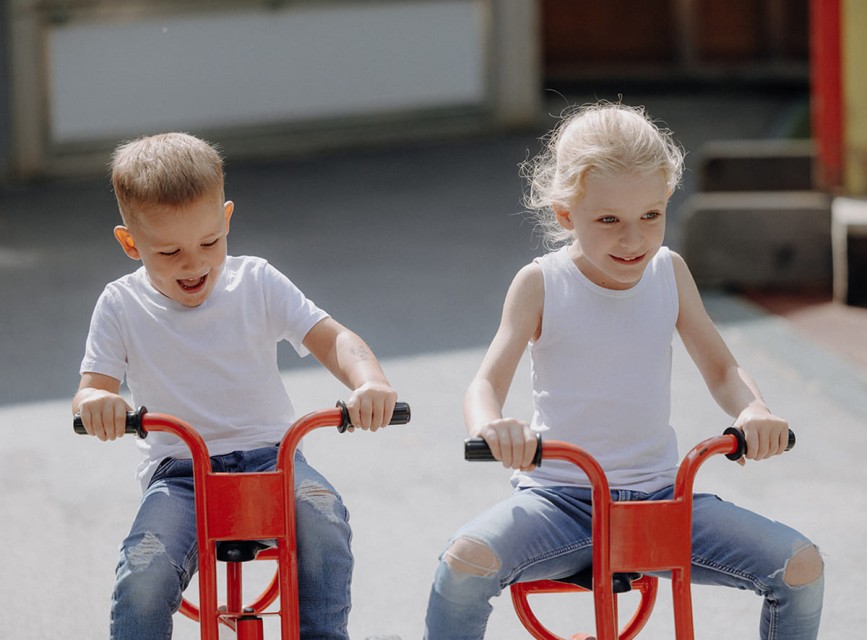 Kinder fahren lachend mit roten Dreirädern am Spielplatz des Hotels Botenwirt