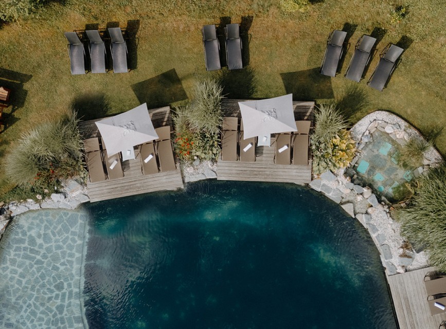 Luftaufnahme des Naturbadeteichs im Hotel Botenwirt mit Liegen und Sonnenschirmen