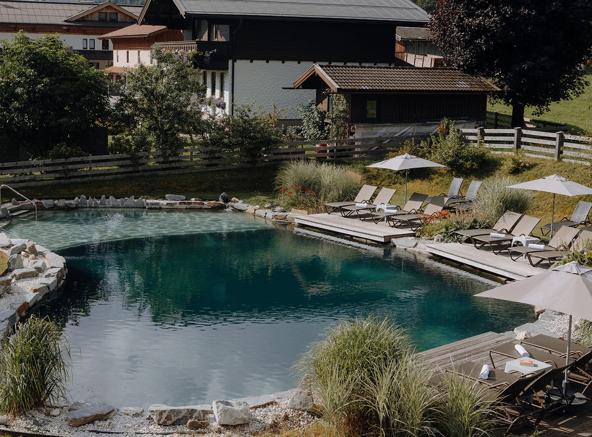 Naturbadeteich im Hotel Botenwirt Kleinarl mit Holzsteg, Sonnenliegen und umliegender Berglandschaft.