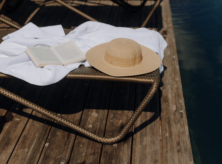 Sommerliche Ruhe am Holzsteg: Liege mit Sonnenhut, Bademantel und ge&ouml;ffnetem Buch direkt am Naturteich