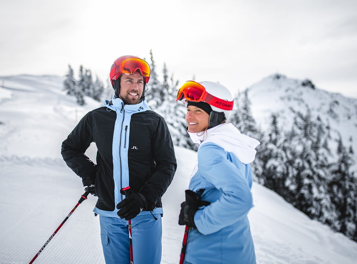 Skifahrer-Paar macht Pause auf der Skipiste mit verschneiter Berglandschaft im Hintergrund &copy; Wagrain-Kleinarl